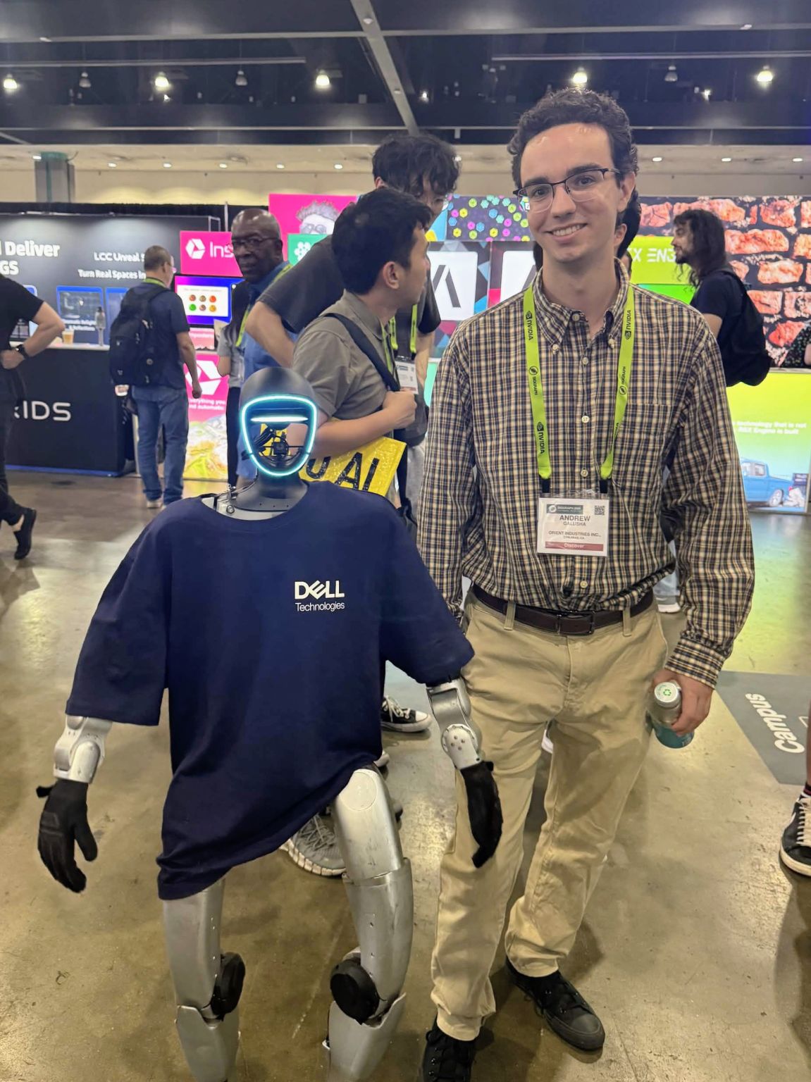 Andrew at SIGGRAPH in a plaid shirt and an NVIDIA lanyard, standing beside Dell's humanoid robot, which wears a navy Dell Technologies T-shirt, on the exhibition floor